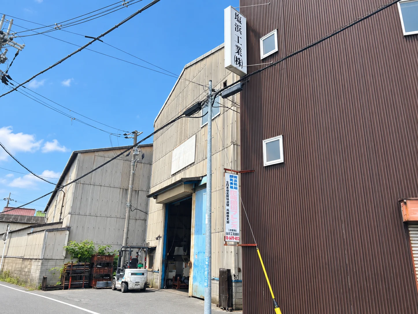 青空の下に建つ塩浜工業の工場外観と看板